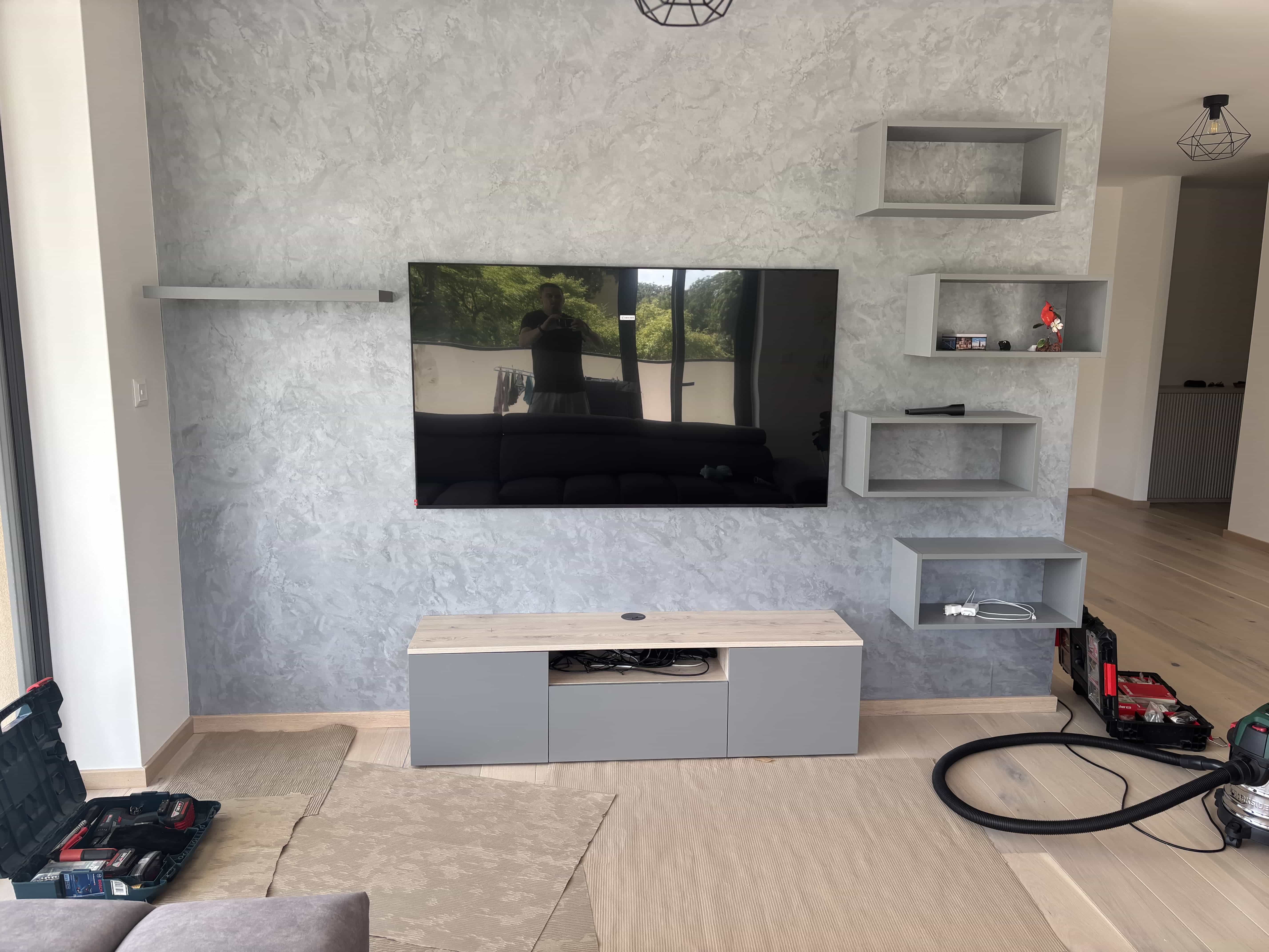TV na designovej stene s dekoračnou omietkou a závesnými policami